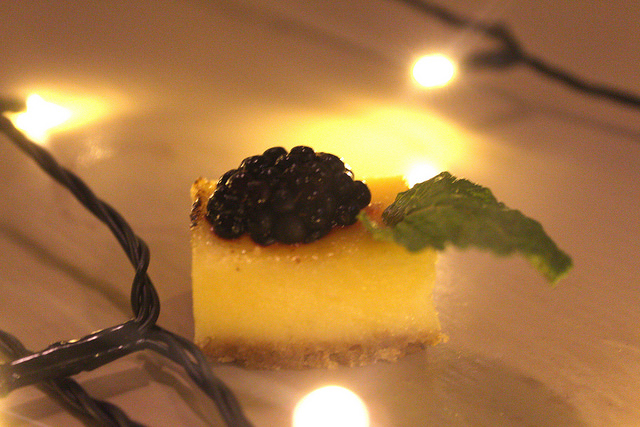 A slice of pale yellow tarte, with some fruit on top, and a sprig of Mint, on a wooden background.
