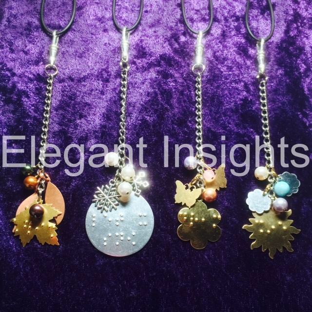 A tan brown maple leaf charm, - silver disco ball shaped charm, a brightly coloured sun charm and a light green butterfly charm all on silver linked chains on a sparkly purple background.
