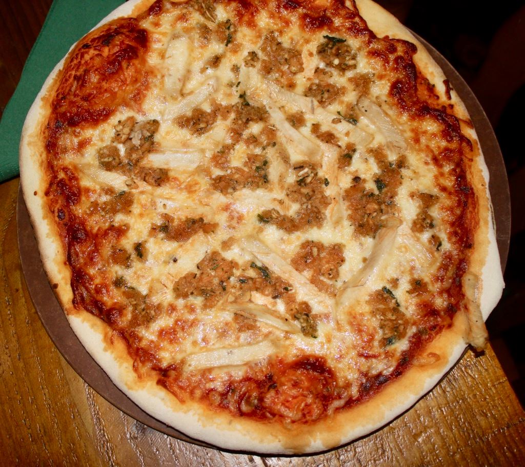 A golden pizza base, topped with a dark red tomato sauce, some tanned cheese, and some dark brown meat and stuffing, on a dark brown background.