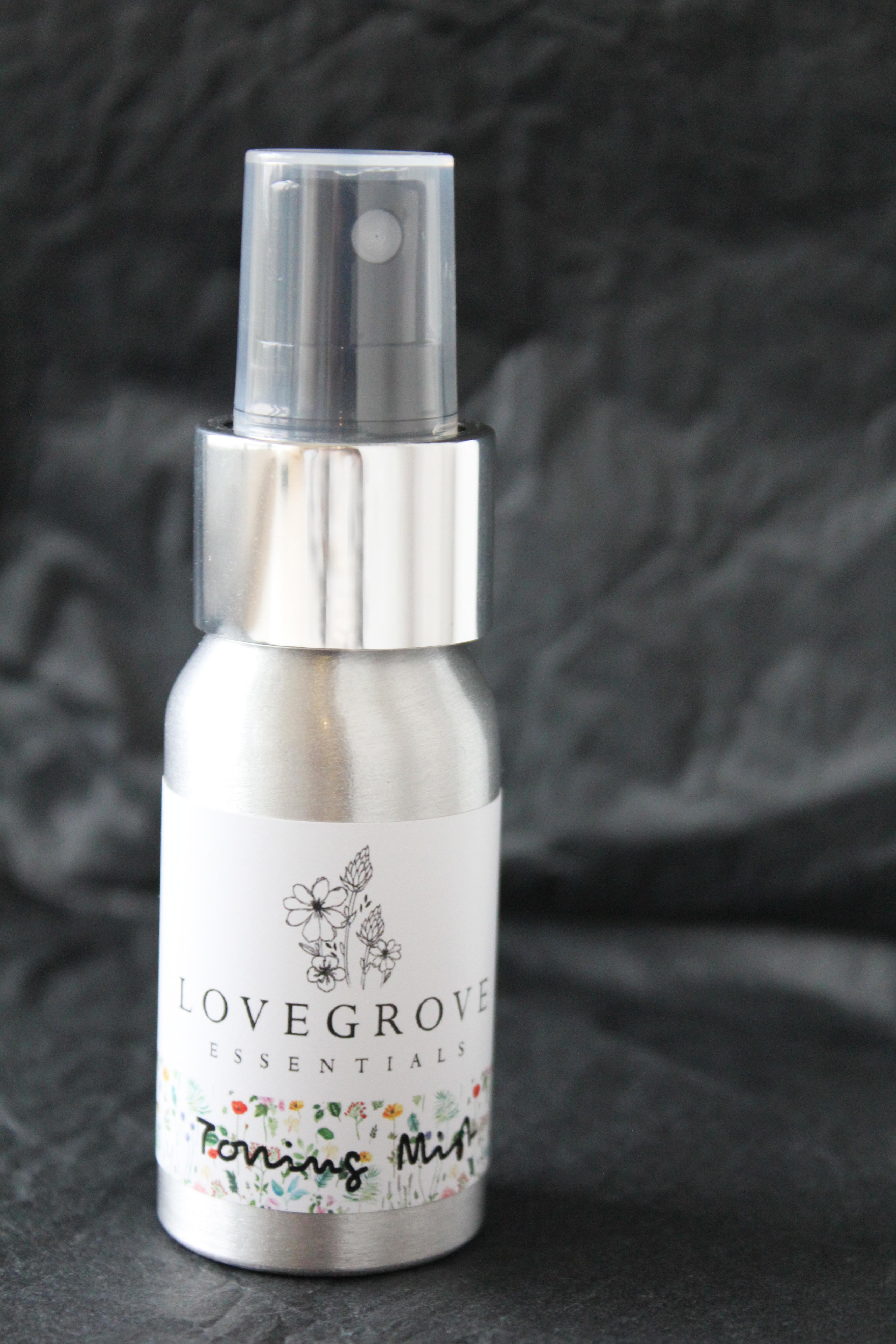 A white tall bottle with a plastic lid, with Lovegrove Essentials toning mist written on the side of it, on a dark background.
