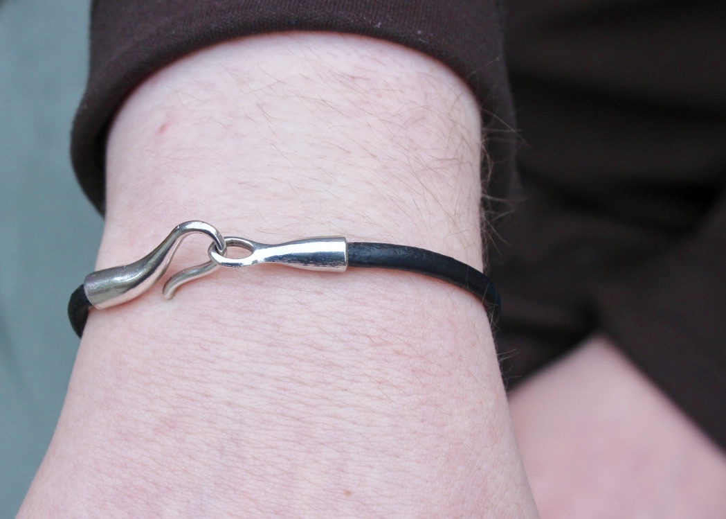 A Black leather hook bracelet on a white arm, on a dark background.