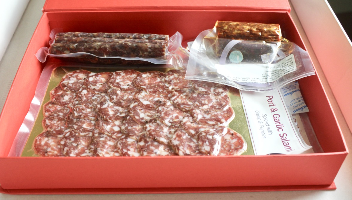 A large red rectangular box containing some different sized packets of different coloured meats, with some white pieces of paper inside the box, on a white background.