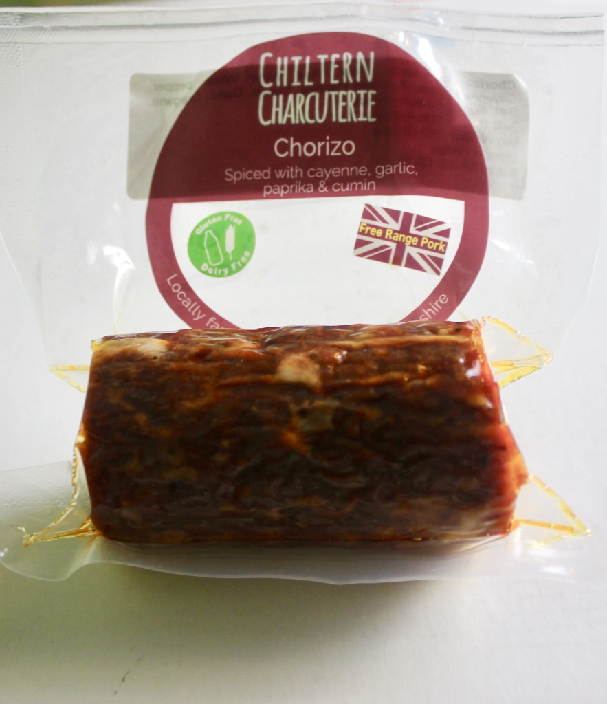Some dark red Chorizo in a large rectangular see through packet with a red, white, and blue Union Jack on top of it, with a red logo and some black text on the packet, on a white background.