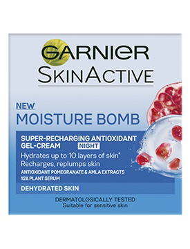 A grey square box with Garnier written in bold black writing with a green circle over the G, New Moisture Bomb written in light blue writing, and Night Cream written in White text, with some Berries and cream on the box, on a white background.