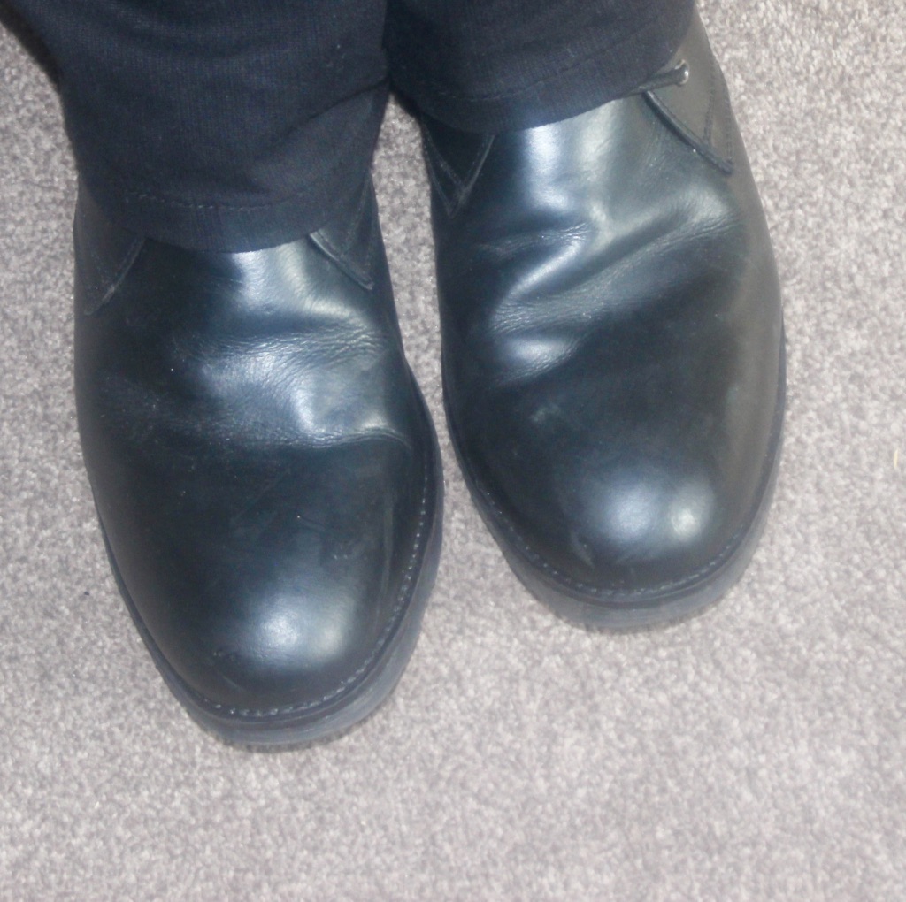 A pair of Black shiny boots, on a beige carpet.