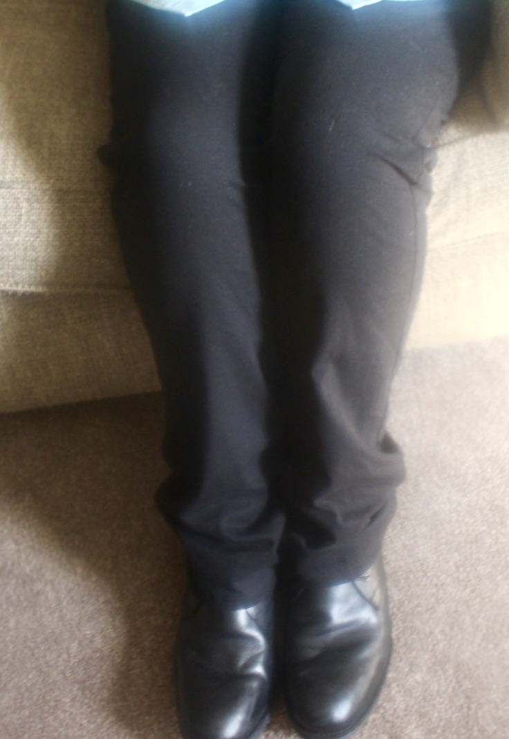 A picture of some black cord trousers, and a pair of black boots, on a beige carpet.