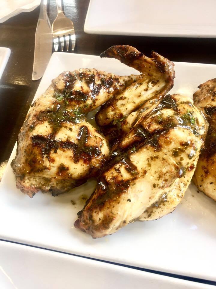 A scorched chicken thigh with brown lines all over it on a white plate, on a dark background.