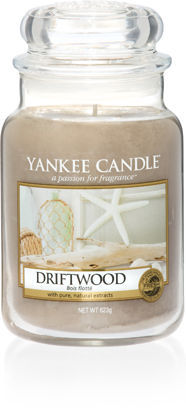 A tall glass jar full of light gold coloured wax, with a label that has a picture of some stars next to some pieces of wood, and Yankee Candle and Driftwood written in black writing on it, on a white background.