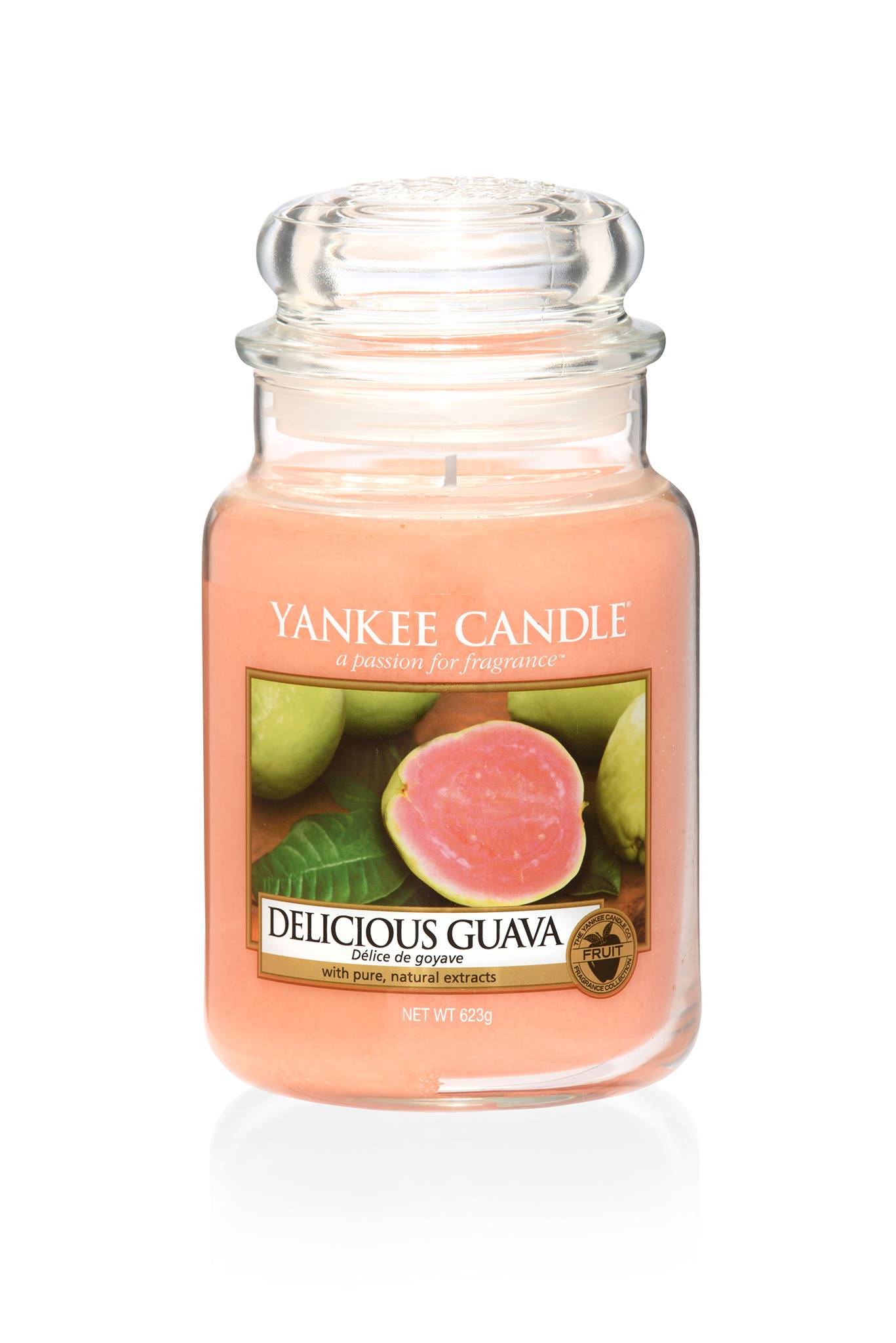 A tall glass jar full of some pastel pink coloured wax, with a label that has yankee candle written in white writing, delicious guava written in black writing, and a picture of some half cut pink Guavas on it, on a white background.