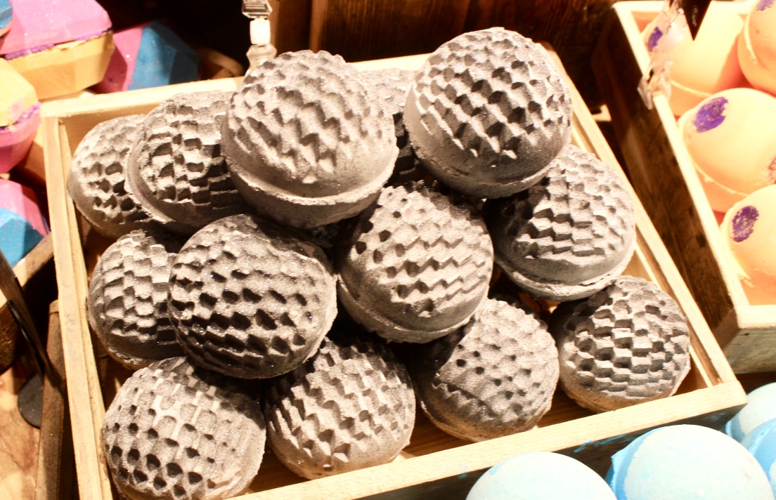 Some grey bath bombs with a prickly spot design all over them in a rectangular light wooden box, on a dark background.