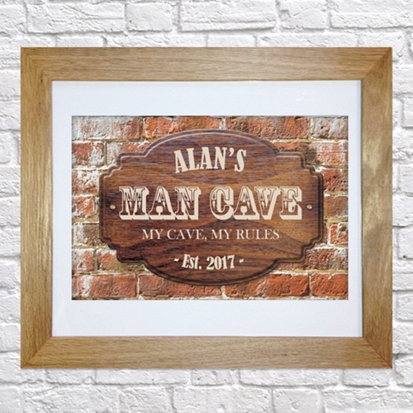 A dark grid printed picture that has Alan's Man Cave written in barber inspired writing and my man cave my rules written in smaller white writing inside a medium coloured wooden frame, on a medium coloured background.
