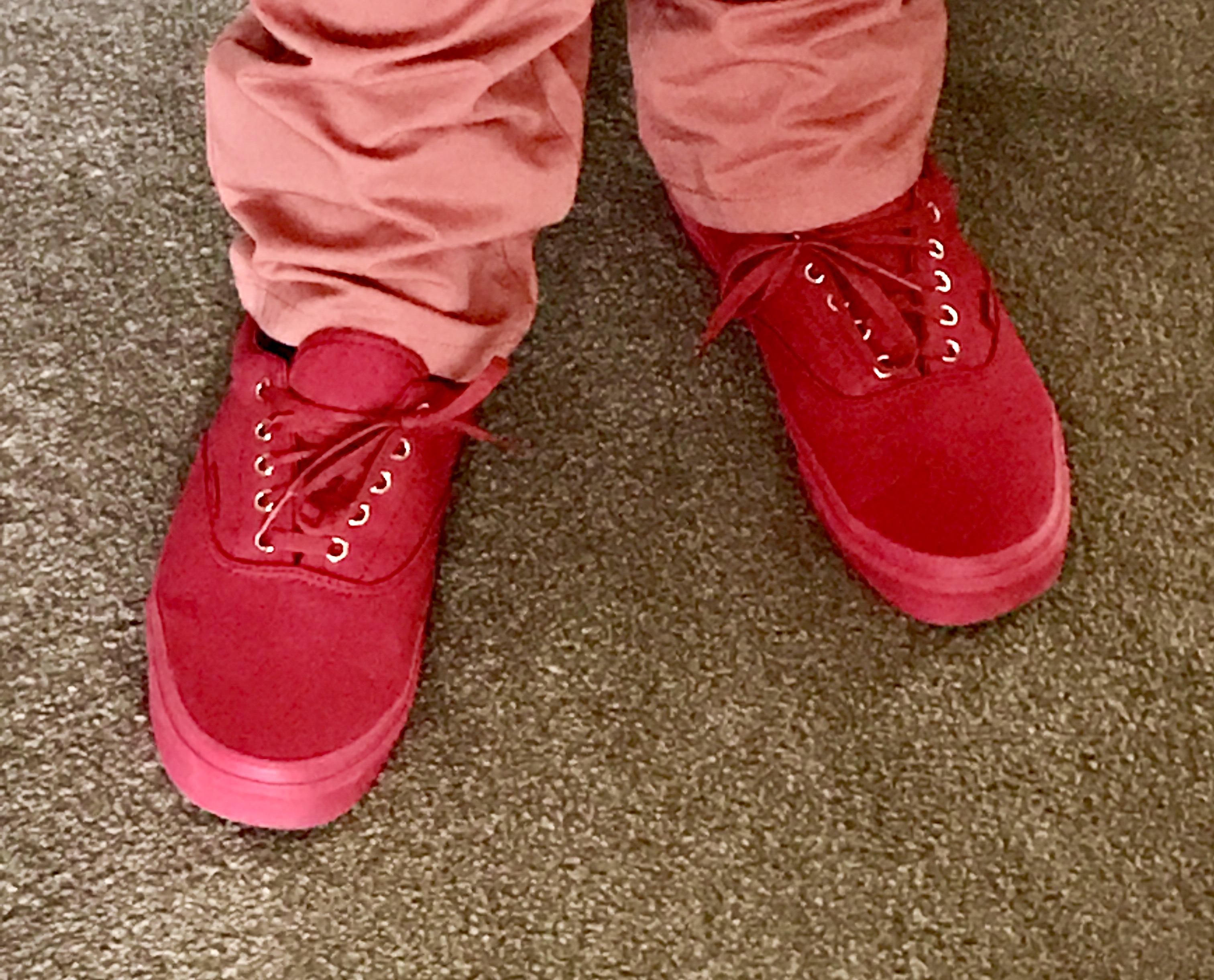 Me wearing a pair of red shoes with some red laces and red soles on a green carpet, on a light background.