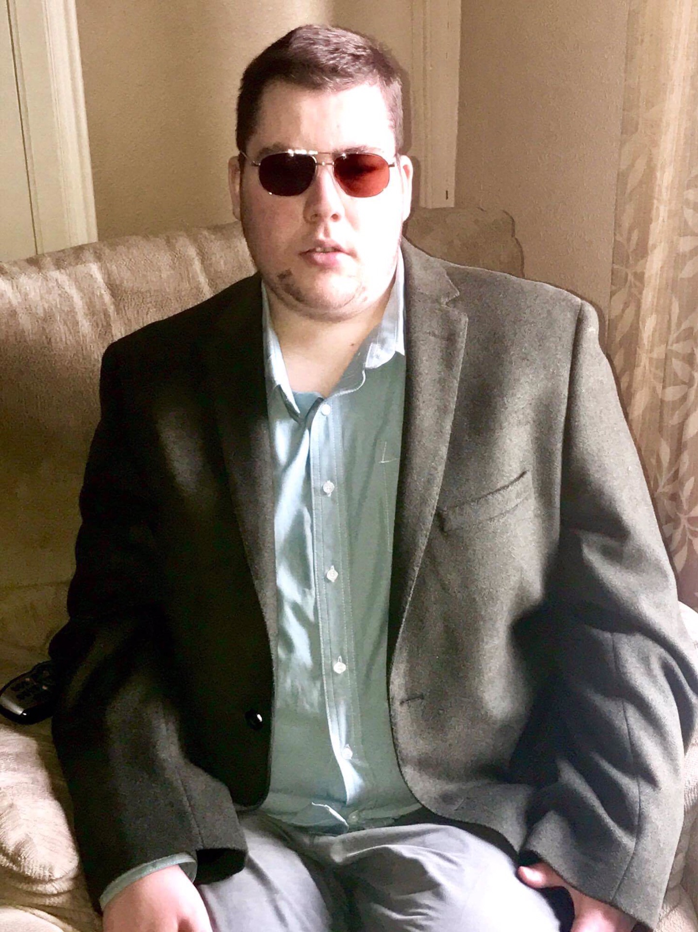 Me sat wearing a dark green blazer and a light green shirt, on a light background.