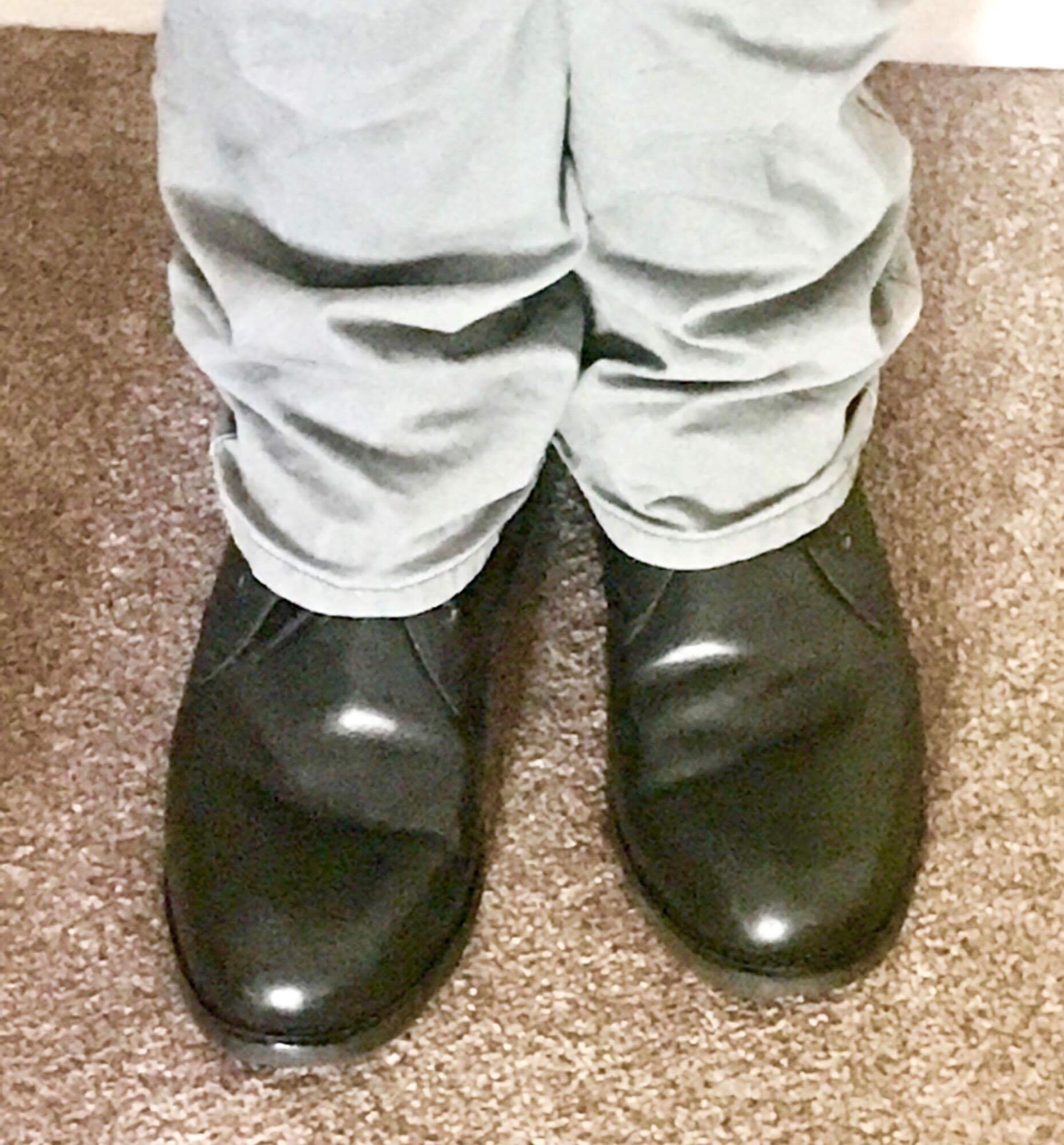 Me wearing a pair of black leather boots on a light brown carpet, on a light background.