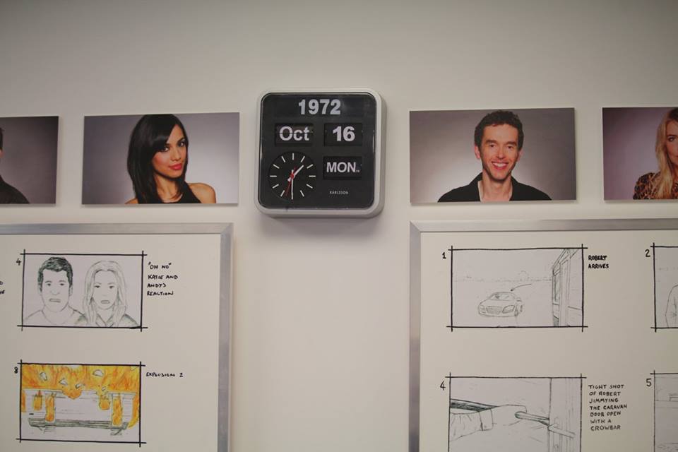 A square black sign that has 1972 October 16 Monday written in white writing on it surrounded by some rectangular pictures of Emmerdale characters and some drawings of actions on a white board, on a white background.