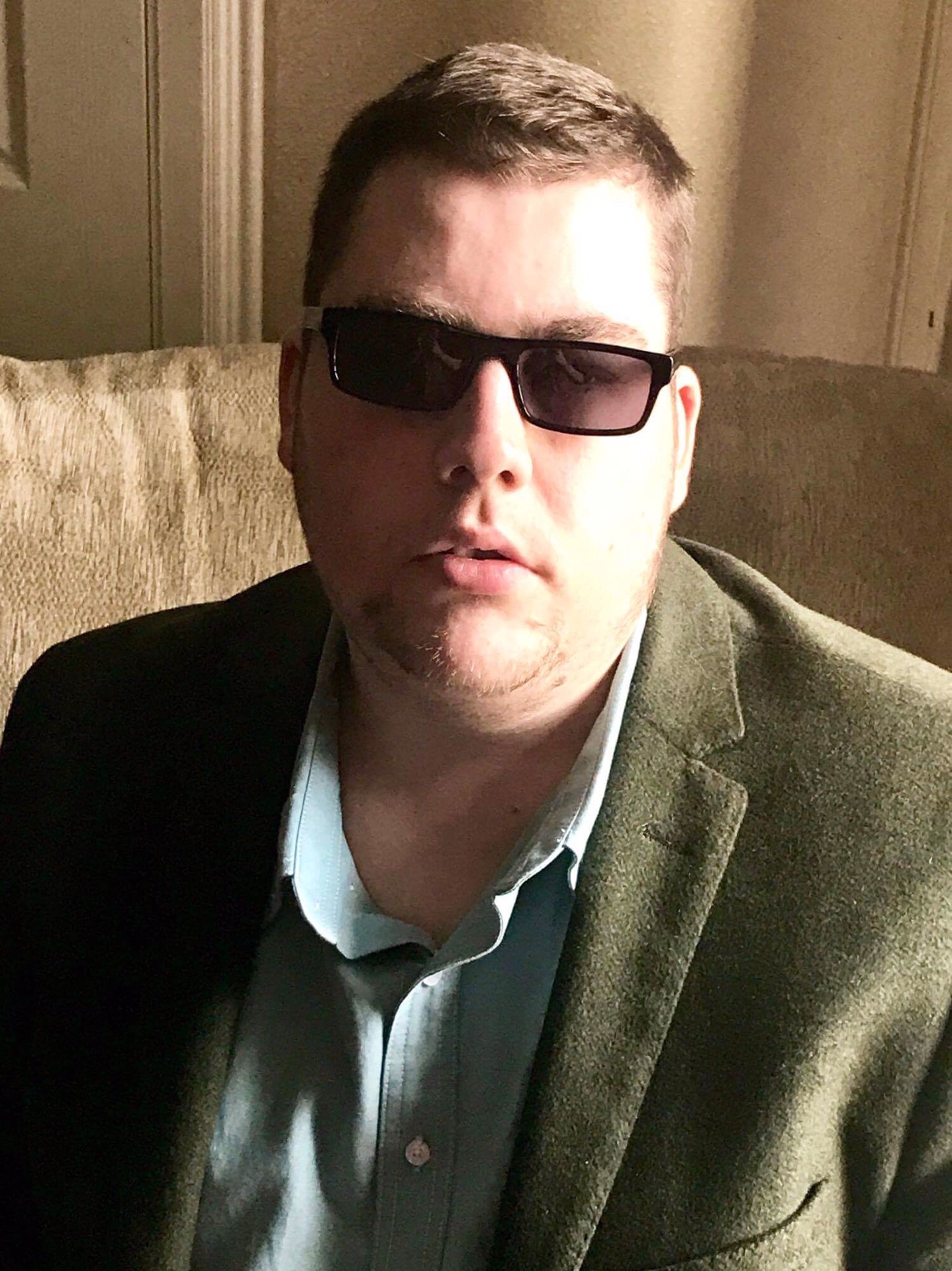 Me wearing a Green blazer, a light Green shirt, and a pair of Black chunky plastic Sunglasses with Grey lenses, on a light background.