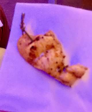 A large piece of crispy golden brown coloured Chicken on a thin wooden skewer on a blue napkin and a white rectangular table, on a light background.