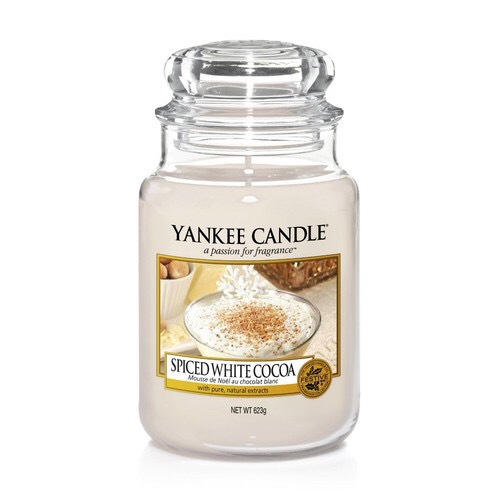 A tall glass jar full of some light white coloured wax with a label that has yankee candle written in white writing, spiced white cocoa written in black writing, and a picture of a white china cup full of some white hot chocolate with a dusting of some golden coloured spices on it, on a white background.