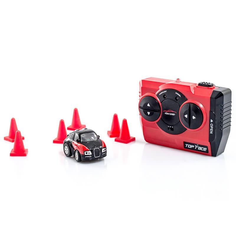 A small Red 4X4 Car with some Black Tyres and White Head Lights next to some bright Orange cones and a large Black and Red remote control, on a white background.