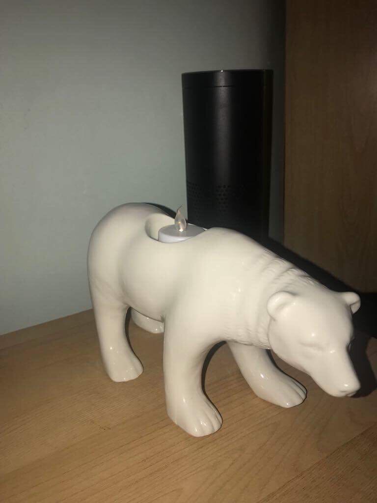 A bright white ceramic polar bear stood on all fours on a light brown rectangular chest of drawers, on a bright background.