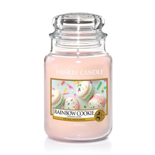 A tall glass jar full of some pastel Green coloured wax with a label that has yankee candle written in black writing, Rainbow Cookie written in black writing, and a picture of some golden cookies with different coloured sprinkles inside a wooden box on it, on a bright background.