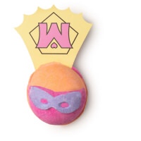 A light yellow spherical shaped bath bomb that has a bright pink crescent and a pair of purple glasses engraved into it and a white piece of paper that has a yellow triangle and a pink M on it attached to the back of it, on a white background.