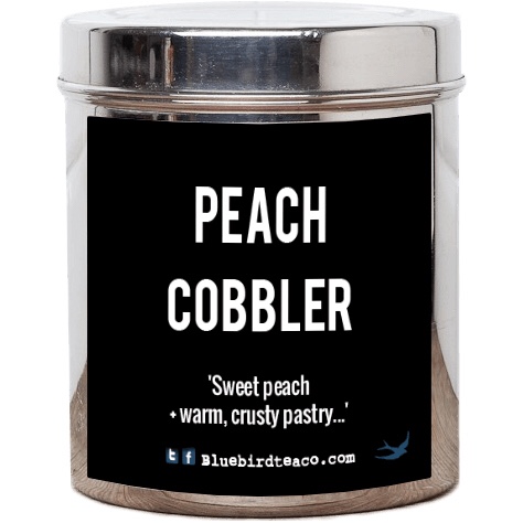A silver metal cylindrical tin that has a black rectangular label, Peach Cobbler written in large bold white writing, and with sweet Peach and warm crusty pastry and bluebirdteaco.com written in smaller white writing on it, on a white background.