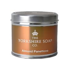 A tall Silver Metal Tin with a white label that has The Yorkshire Soap Company Almond Panettone Tin Candle written in bold black writing on it, on a white background.