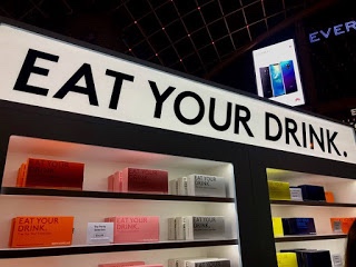 A tall wide white rectangular board that has eat your drink written in bold black writing on it, on a dark background.