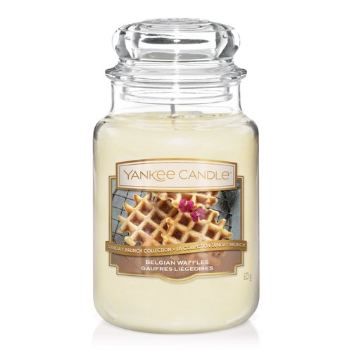 A tall glass jar full of some bright white wax with a label that has Yankee Candle written in gold writing, belgian waffles written in white writing, and a picture of a belgian waffle on it, on a white background.