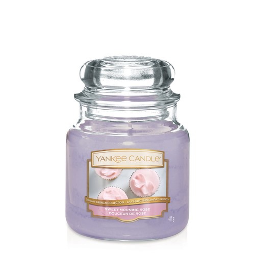 A tall glass jar full of some bright pink wax with a label that has Yankee Candle written in gold writing, blushed bouquet written in white writing, and a picture of some pink flowers on it, on a white background.