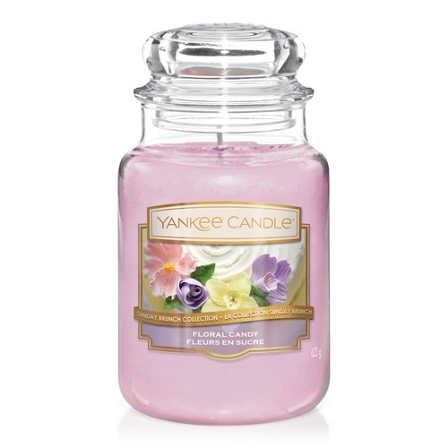 A tall glass jar full of some dark pinky purple wax with a label that has Yankee Candle written in gold writing, floral candy written in white writing, and a picture of some different coloured flowers on it, on a white background.