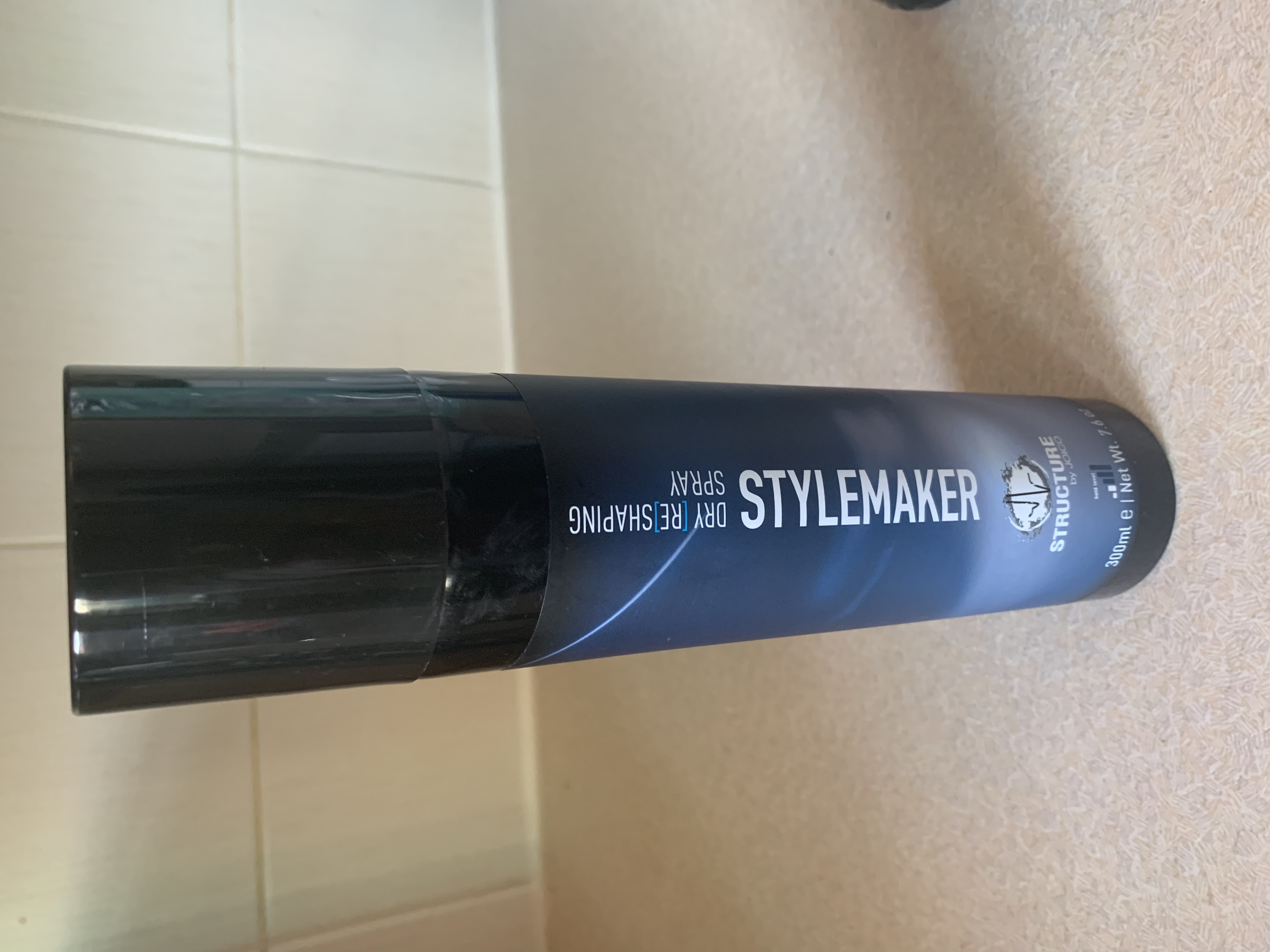 a tall cylindrical Black Plastic Hairspray Can with a white label that has Structure by Joico Stylemaker written in dark blue writing on it, on a white background.