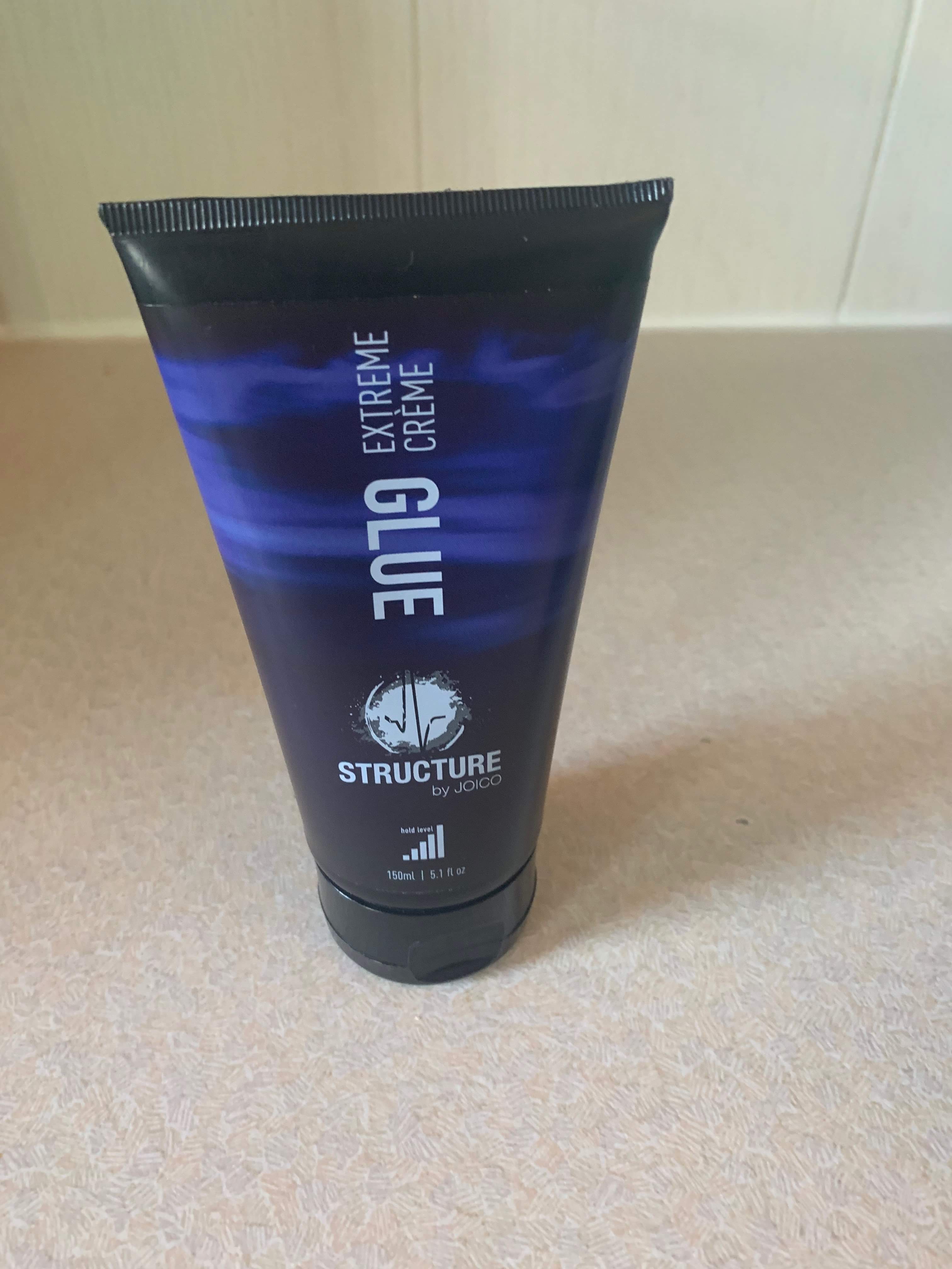 A tall conical shaped tube with a green label that has Structure by Joico Glue written in dark blue writing on it, on a white background.