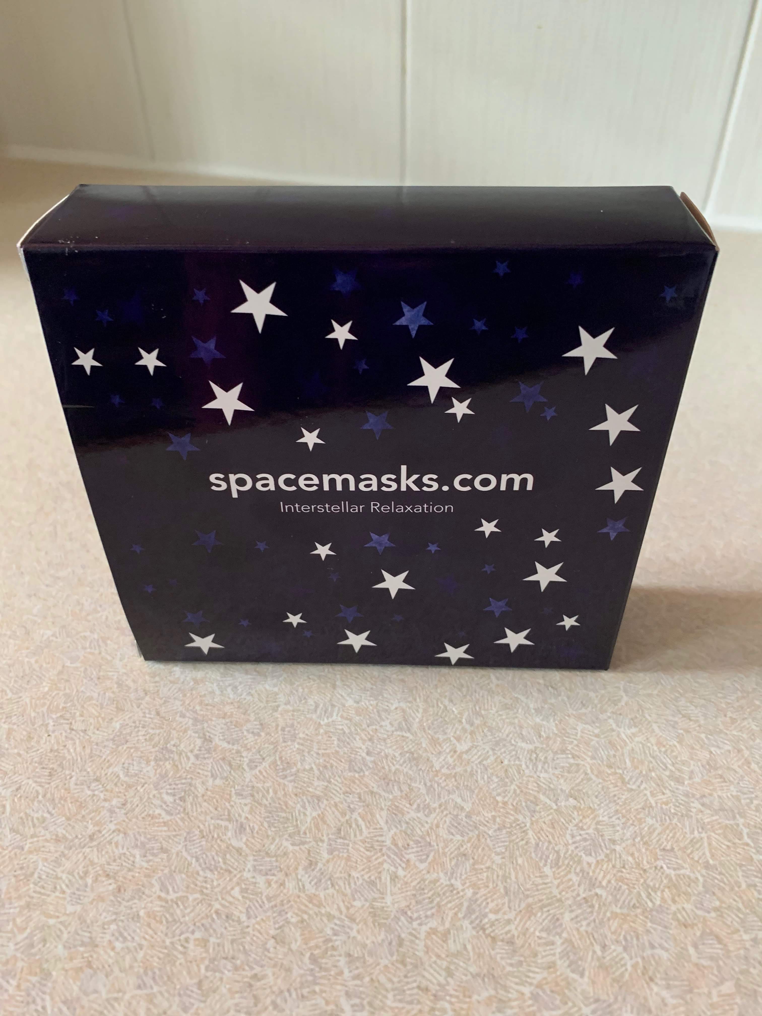 A small rectangular blue cardboard box that has spacemasks written in bold white writing and a picture of some blue and white stars on it, on a white background.