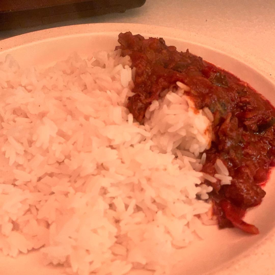 Some pieces of dark brown beef and some crispy vegetables covered in some dark brown sauce on top of some white fluffy rice on a large oval white plate on a white worktop, on a white background.