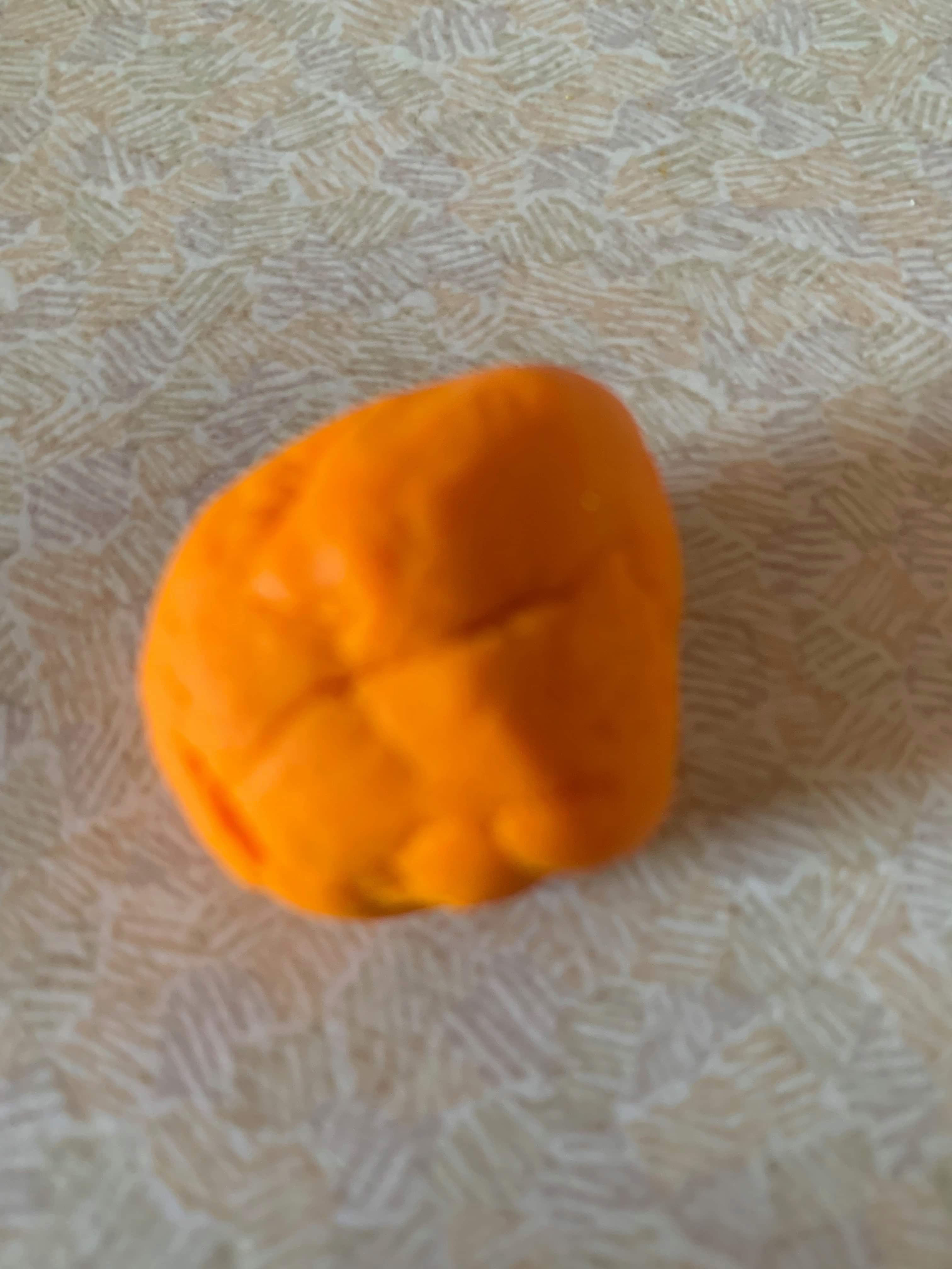 A large circular blob of bright orange plasticine, on a white background.