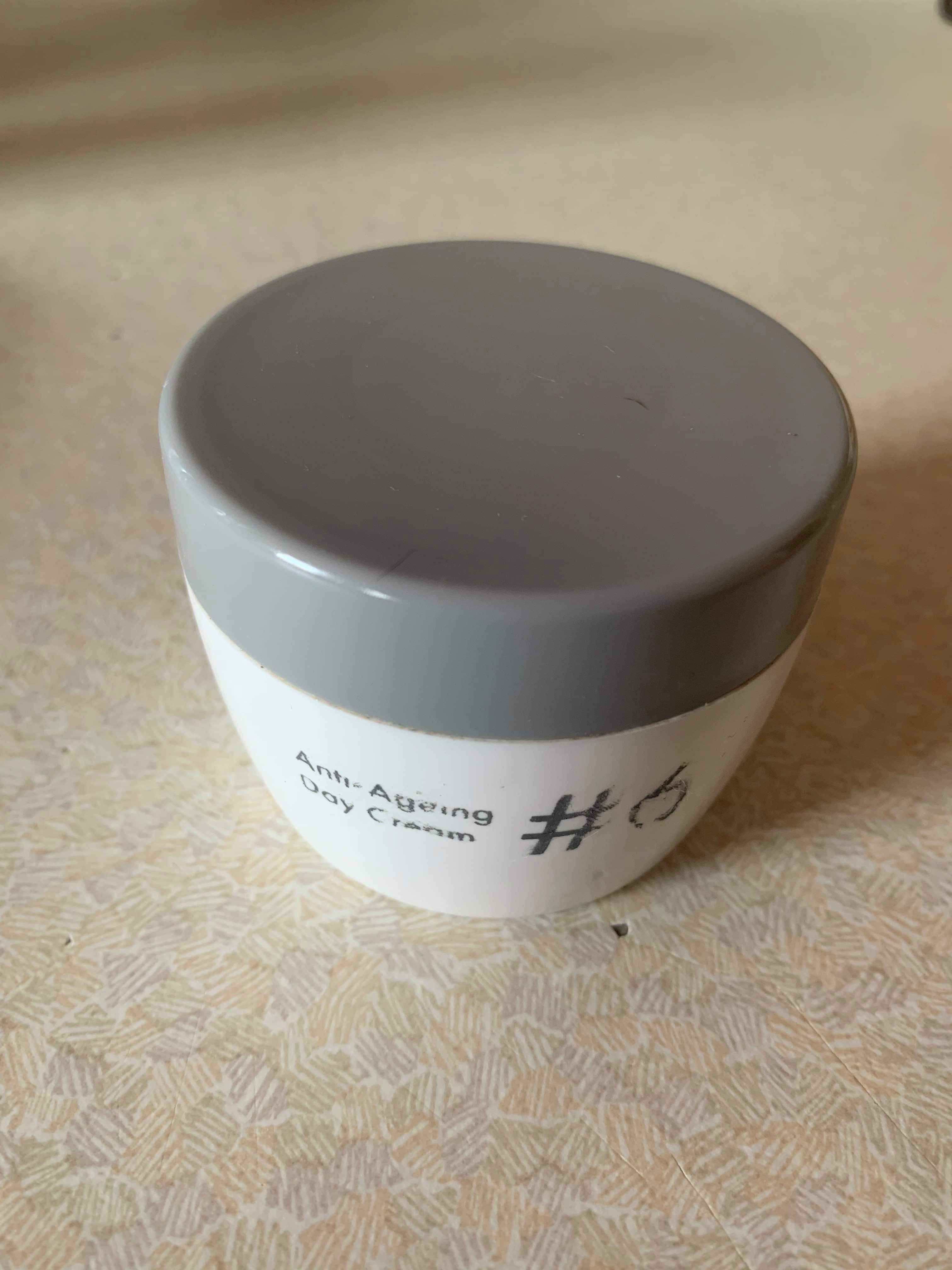 A short cylindrical glossy white plastic tub that has Poundland #6 Anti-Ageing Day Cream written in bold black writing on it, on a white background.