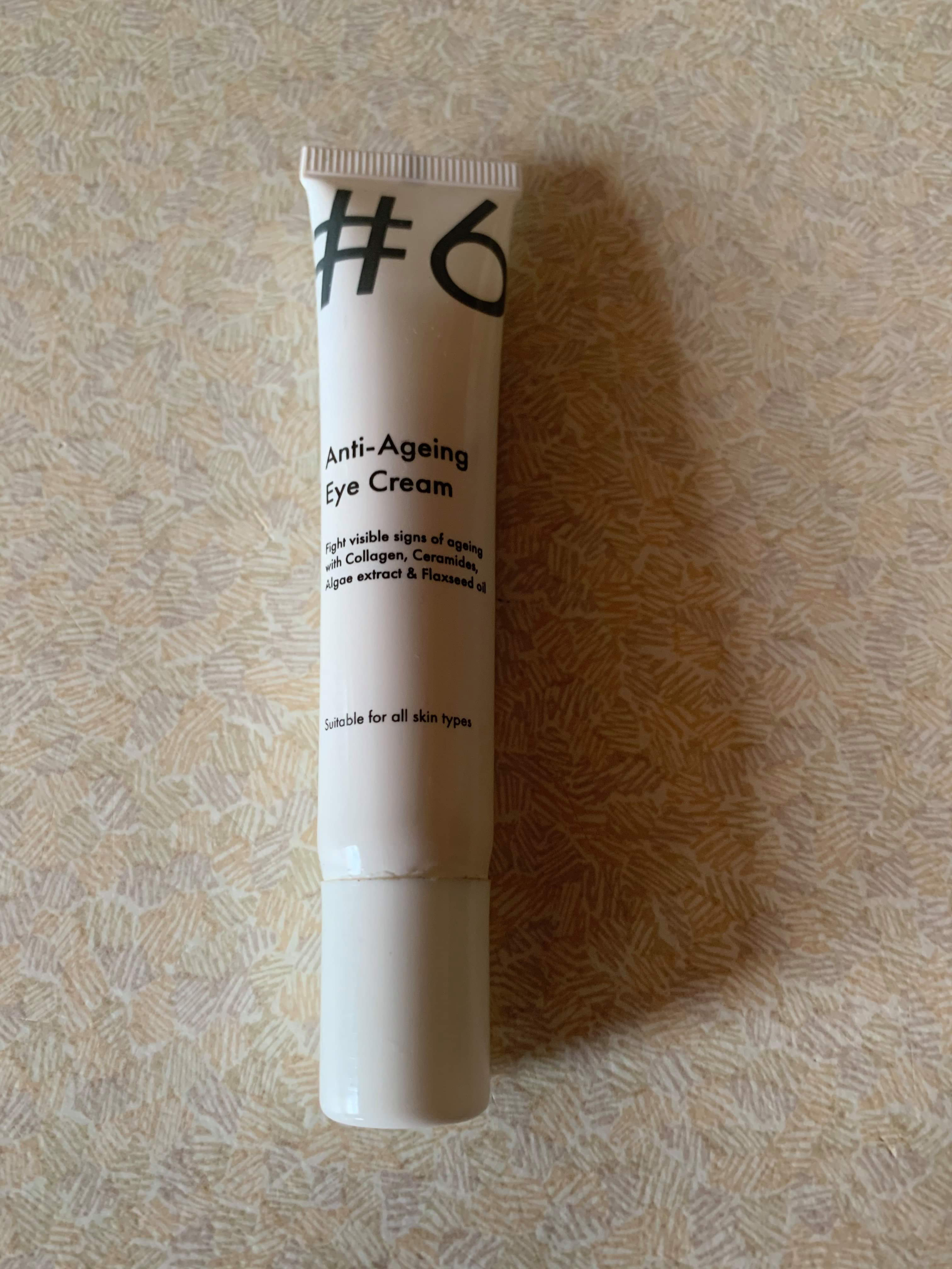 A short thin flat conical glossy white plastic tube that has Poundland #6 Anti-Ageing Eye Cream written in bold black writing on it, on a white background.