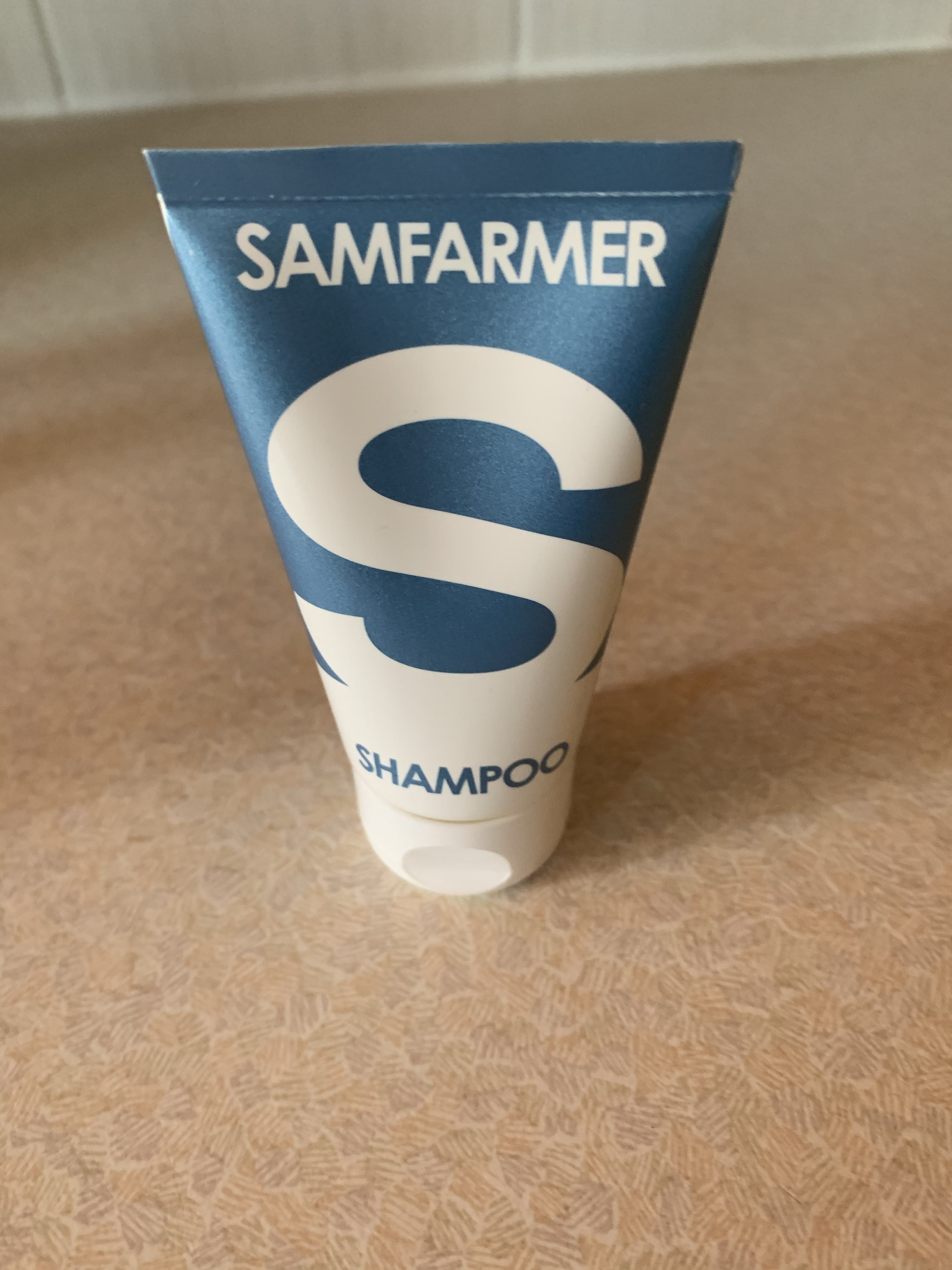 A short flat conical bright orange and white plastic tube that has Sam Farmer written in bold white writing and Conditioner written in bright orange writing on it, on a white background.