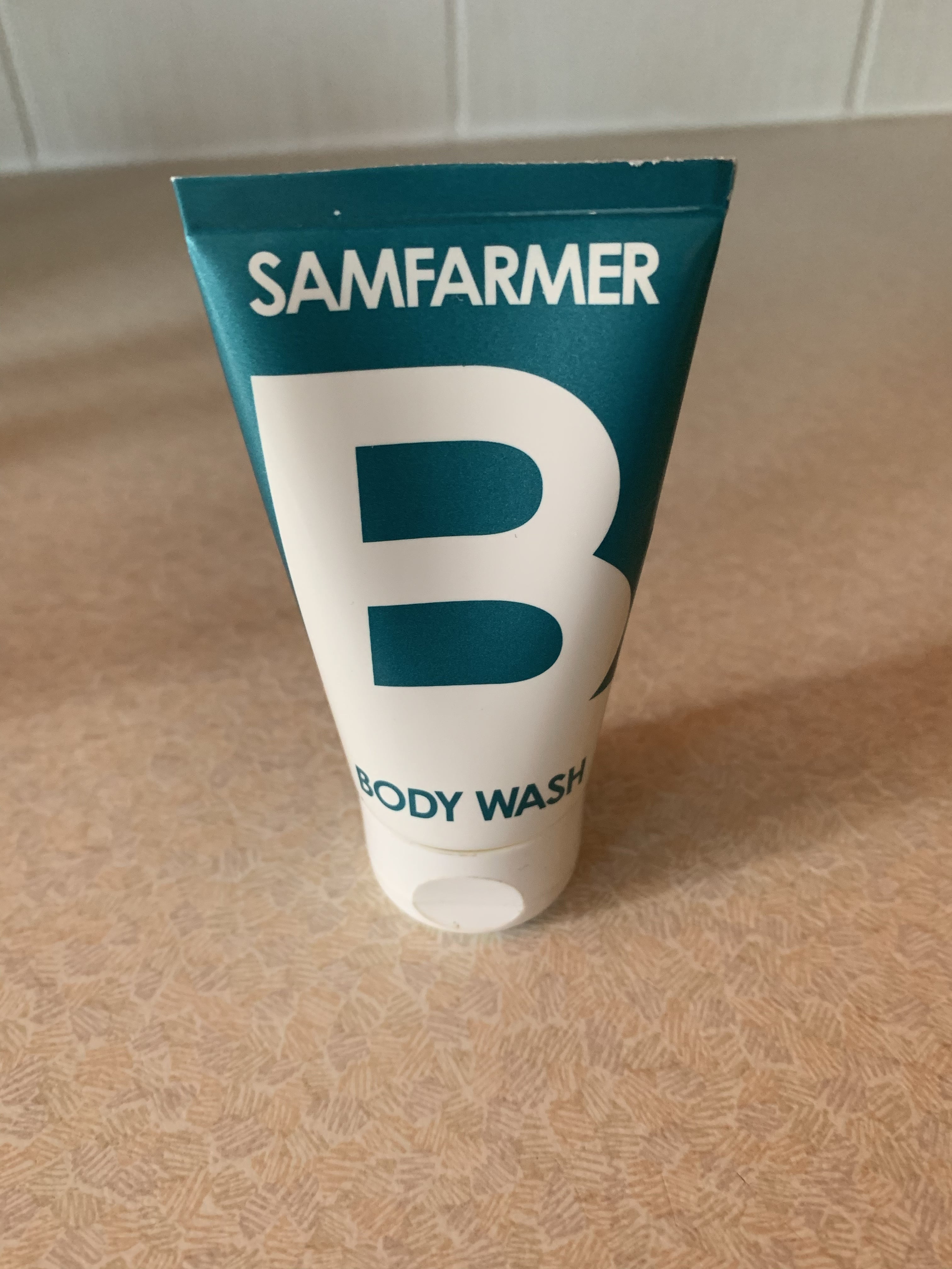 A short flat conical light blue and white plastic tube that has Sam Farmer written in bold white writing and Shampoo written in light blue writing on it, on a white background.