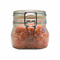 A large octagonal shaped glass mason jar full of some dark orange body scrub with a silver metal lever clasp, on a white background.