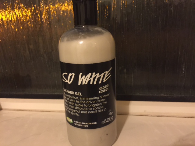 A tall cylindrical clear plastic bottle full of some shimmering Green liquid with a label that has So White Shower Gel written in bold black writing on it, on a white background.