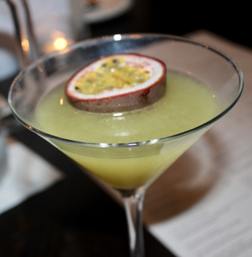 A clear wide glass full of Passion Fruit and Peach Daiquiri, with a purple Passion Fruit garnish floating in the glass, on a grainy background.