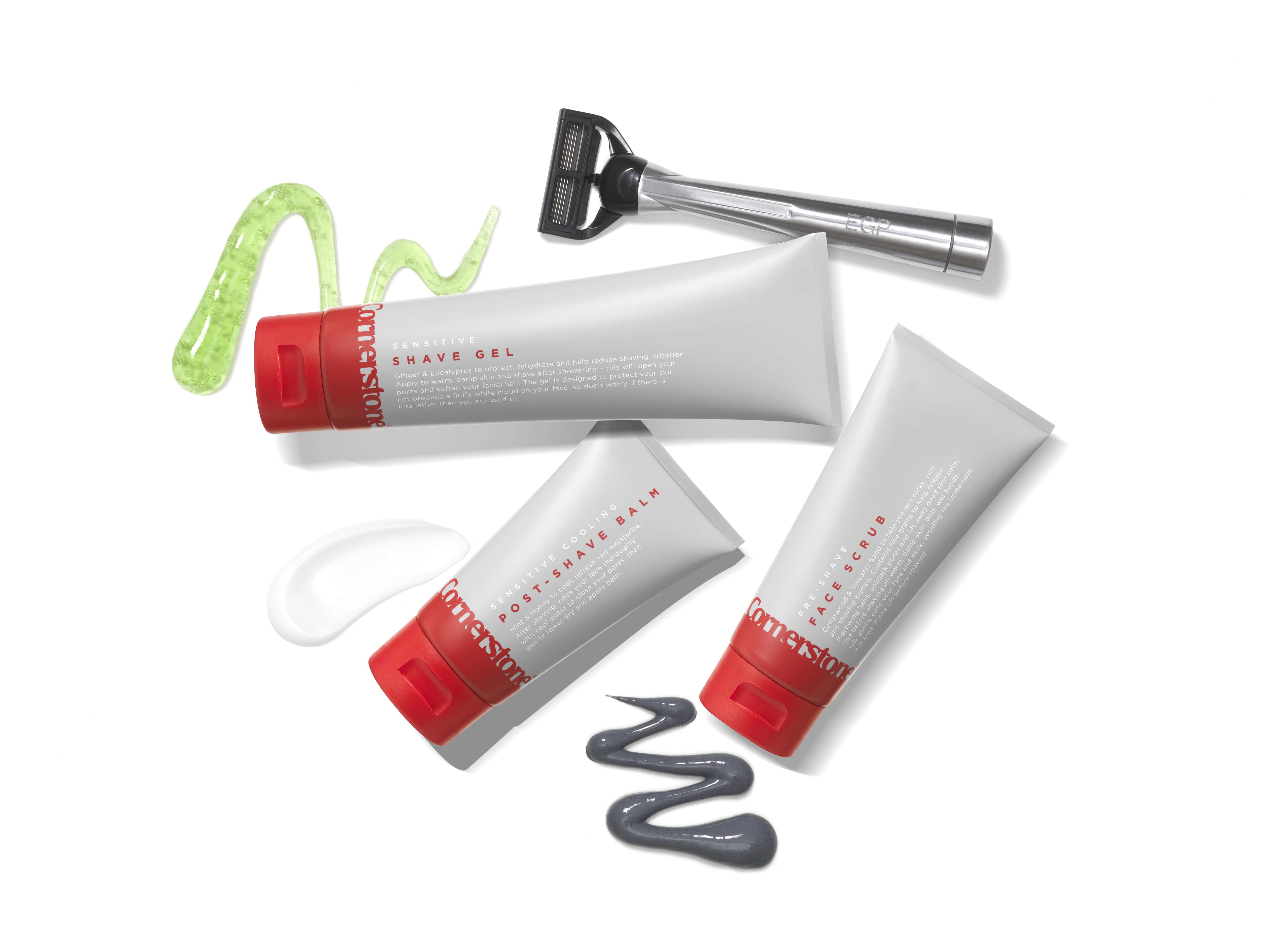The Bluebeards Revenge Cooling Moisturiser, Luxury Shaving Cream, and Post Shave Balm Three bottles with cornerstone printed on the front of them, with red lids, with a metal engraved razor next to them, on a white background.