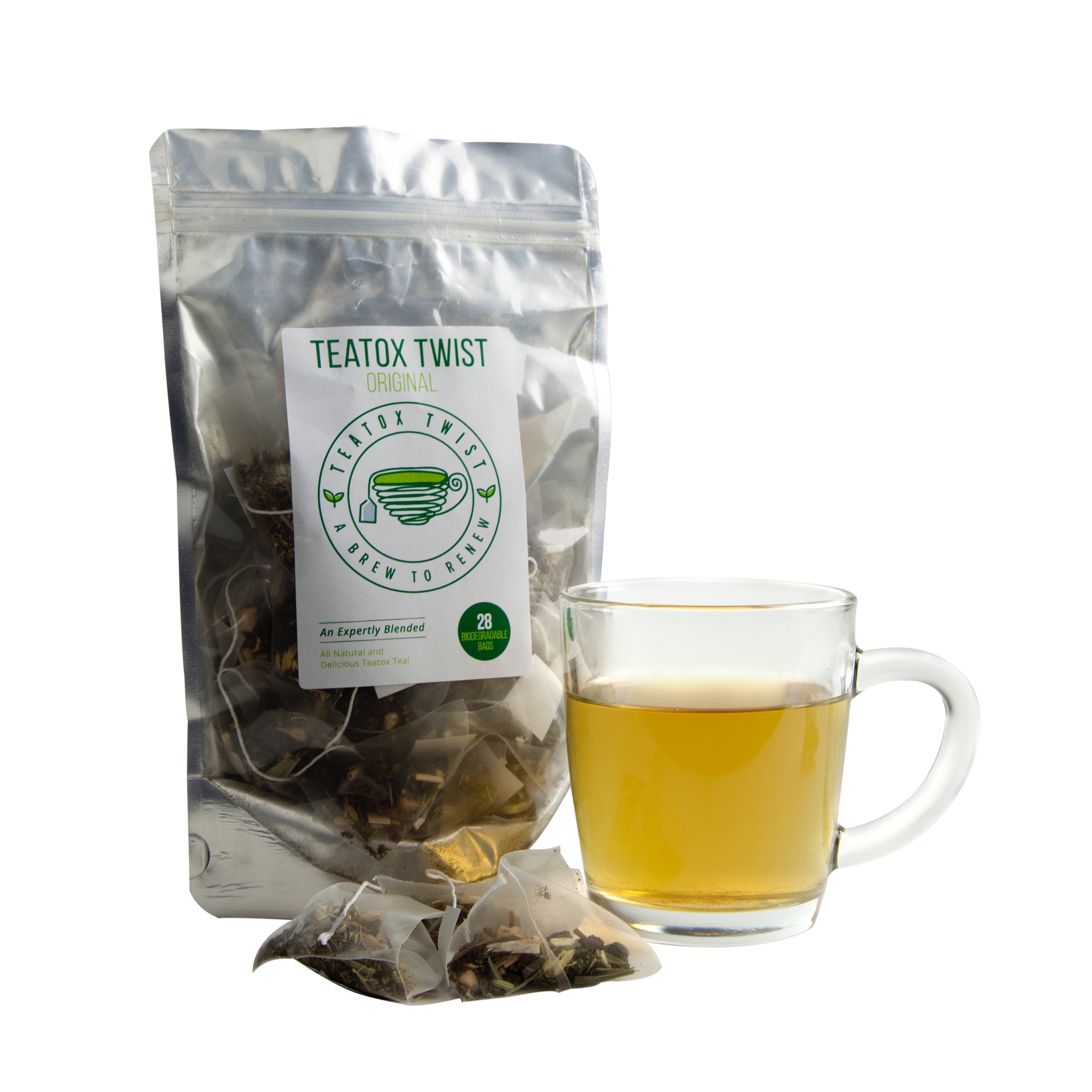 A large silver coloured plastic pouch with a white label that says Teatox Twist in black writing on it, with some green pyramid teabags in front of the pouch, and a large glass mug with some golden coloured liquid in it next to the pouch, on a white background.