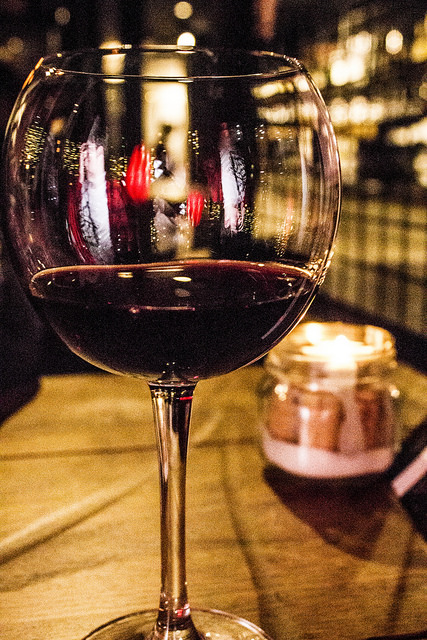 Sweet, Sugar, Candy Man! | Smith & Sinclair Leeds Pop Up Store Launch with The Alchemist Trinity Leeds A tall wide wine glass containing some dark Red wine on a wooden table with a bright square candle in the background, on a light background.