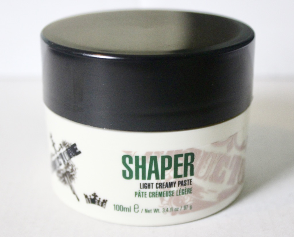 The Structure Of Good Hair | STRUCTURE Shaper Light Creamy Paste A gold cylindrical tub with a black lid, that has Shaper written in large black writing and light creamy paste written in small black writing on a gold label,, on a white background.