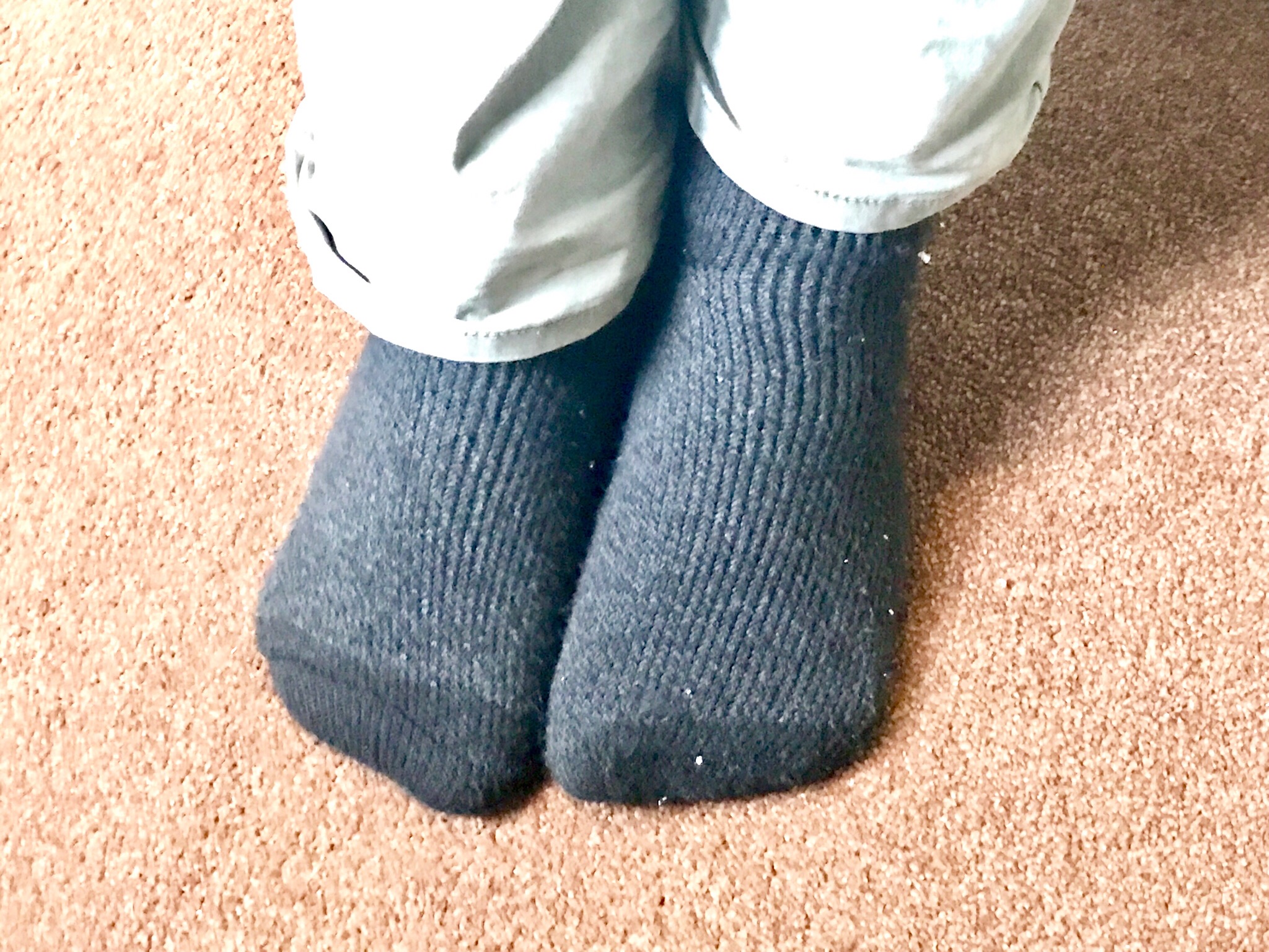 A person wearing a pair of Black socks that has a thick horizontal white stripe and a thinner bright Red stripe at the ankle, on a bright background.