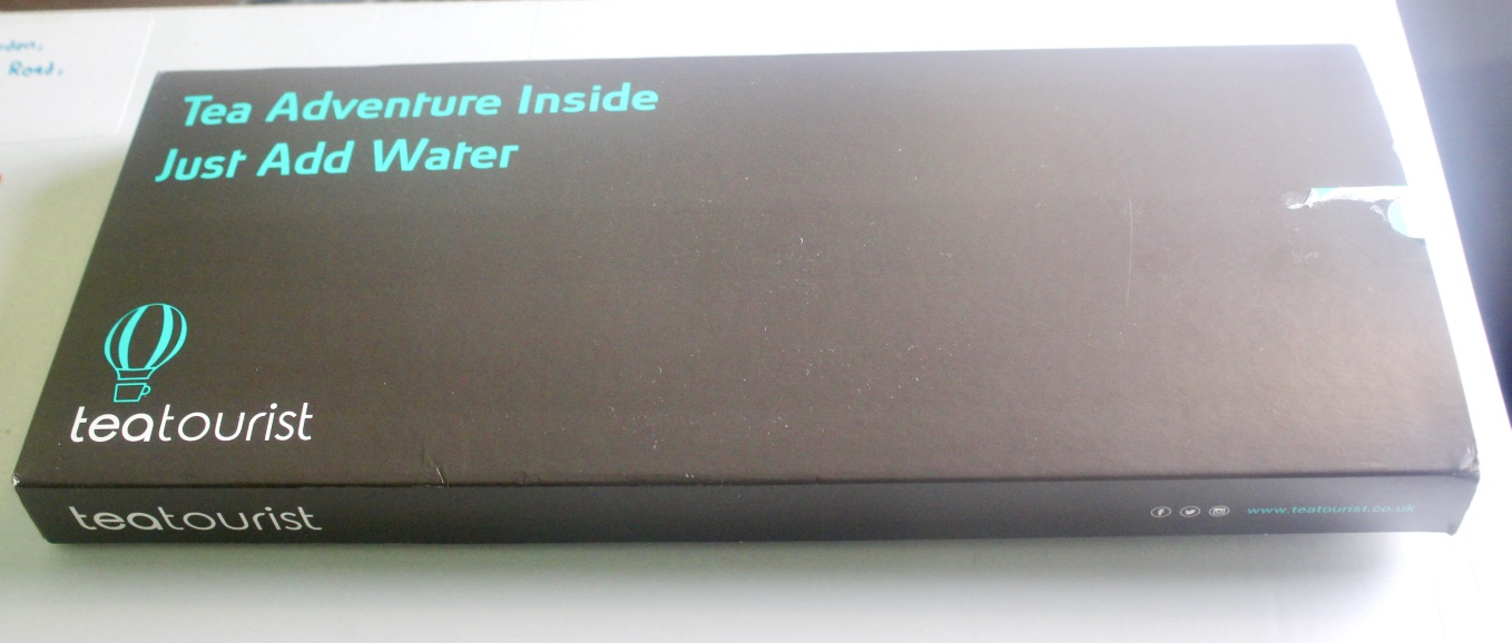 Tea Tastes Terrific | Teatourist April 2017 A long rectangular dark grey and black box with a sticker that has Tea Adventure Inside Just Add Water written in bold white writing on it in the upper left corner and the teatourist logo in the bottom right corner, on a white background.